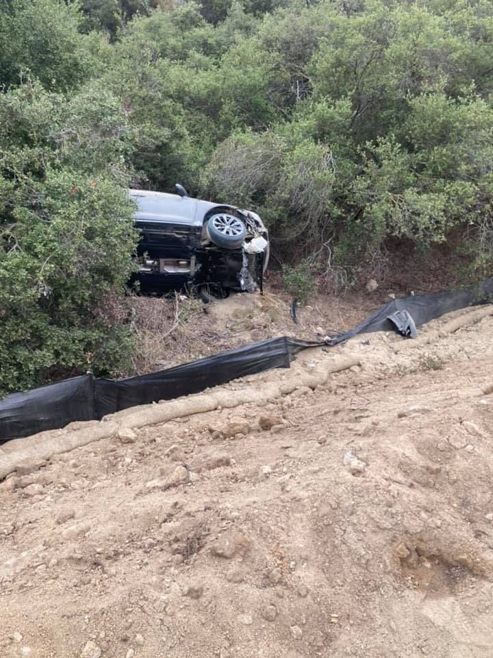Car crashed off road in a dirt embankment, surrounded by trees.