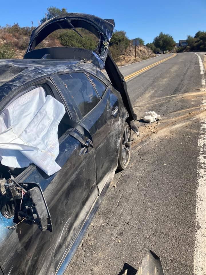 Black car severely damaged after an accident on a rural road; airbags deployed.