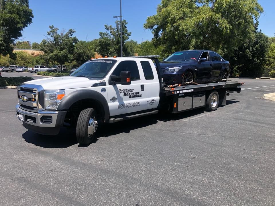 Dark brown vintage pickup truck on a flatbed tow truck, chrome grill, low profile tires, dusk setting.
