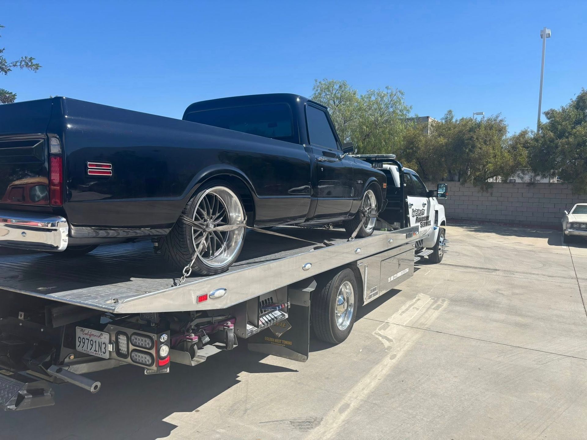 Black classic pickup truck on a flatbed tow truck on a sunny day.