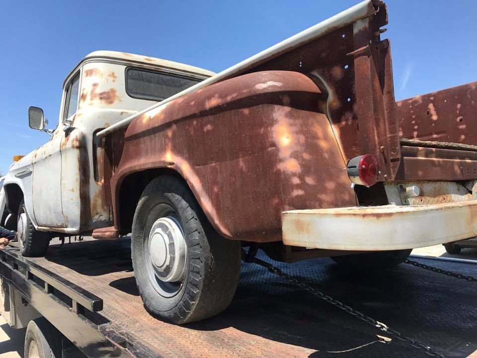 Rusty white vintage truck on a flatbed tow truck, against a clear blue sky.
