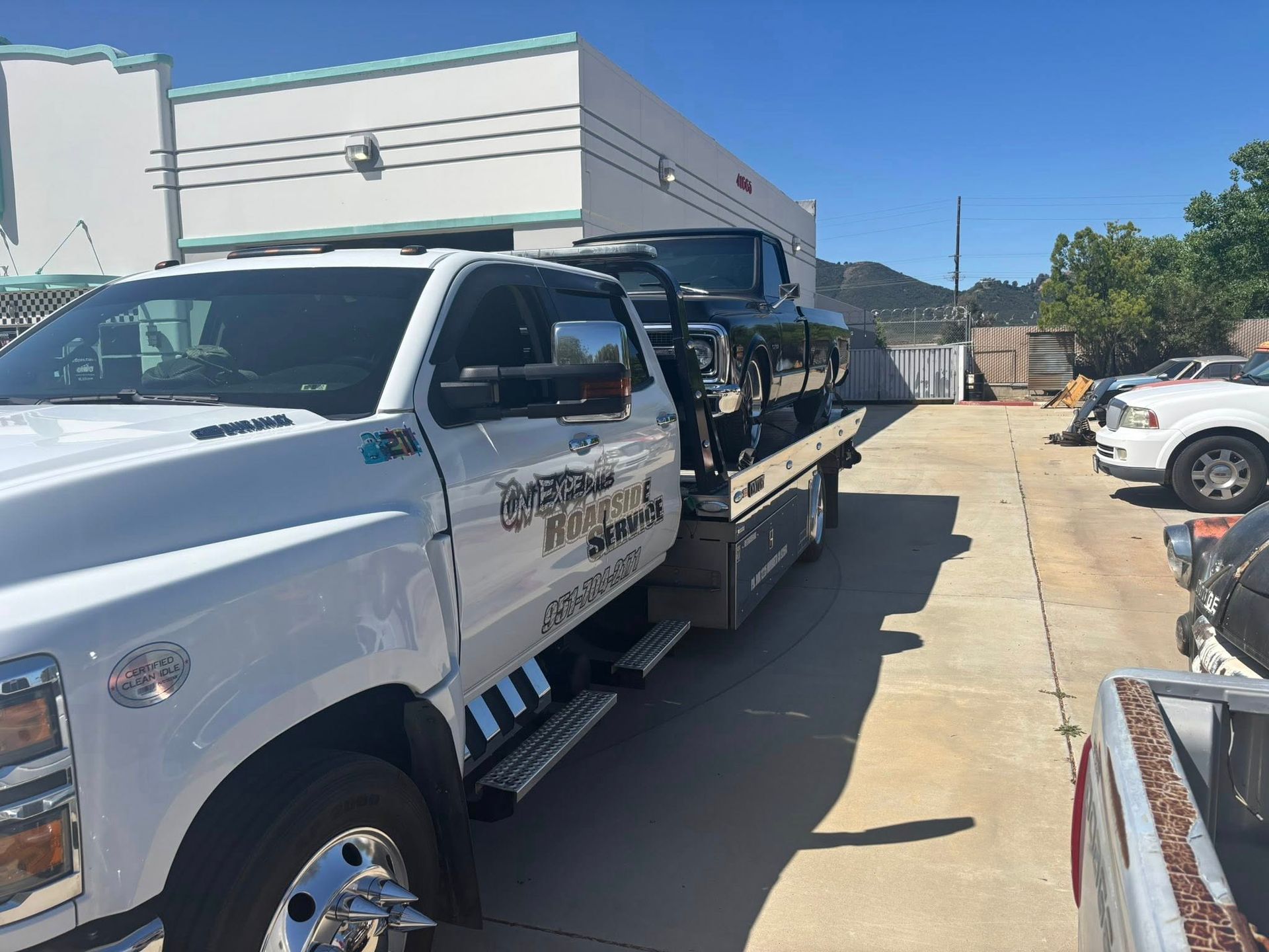 White tow truck with a black car on its flatbed in a parking lot.