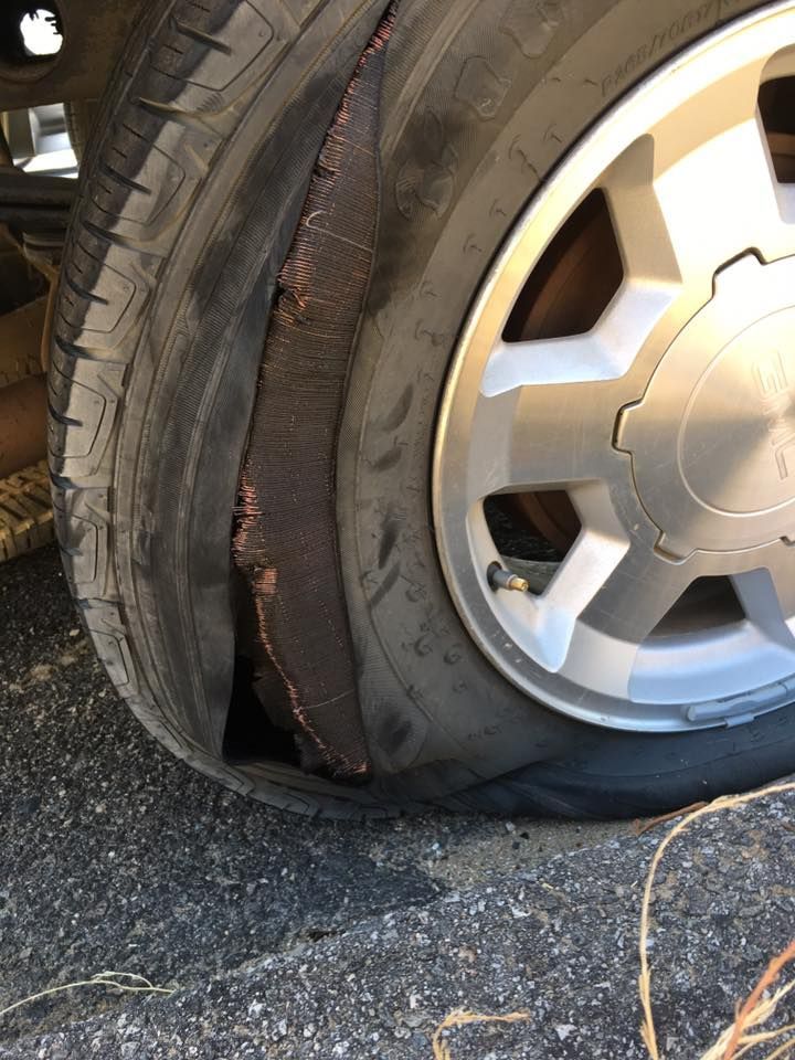 Damaged car tire with a large gash exposing the tire's inner structure, on an asphalt surface.