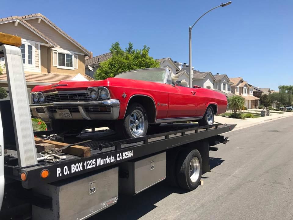 Red convertible classic car on a tow truck on a sunny street in Murrieta, California.