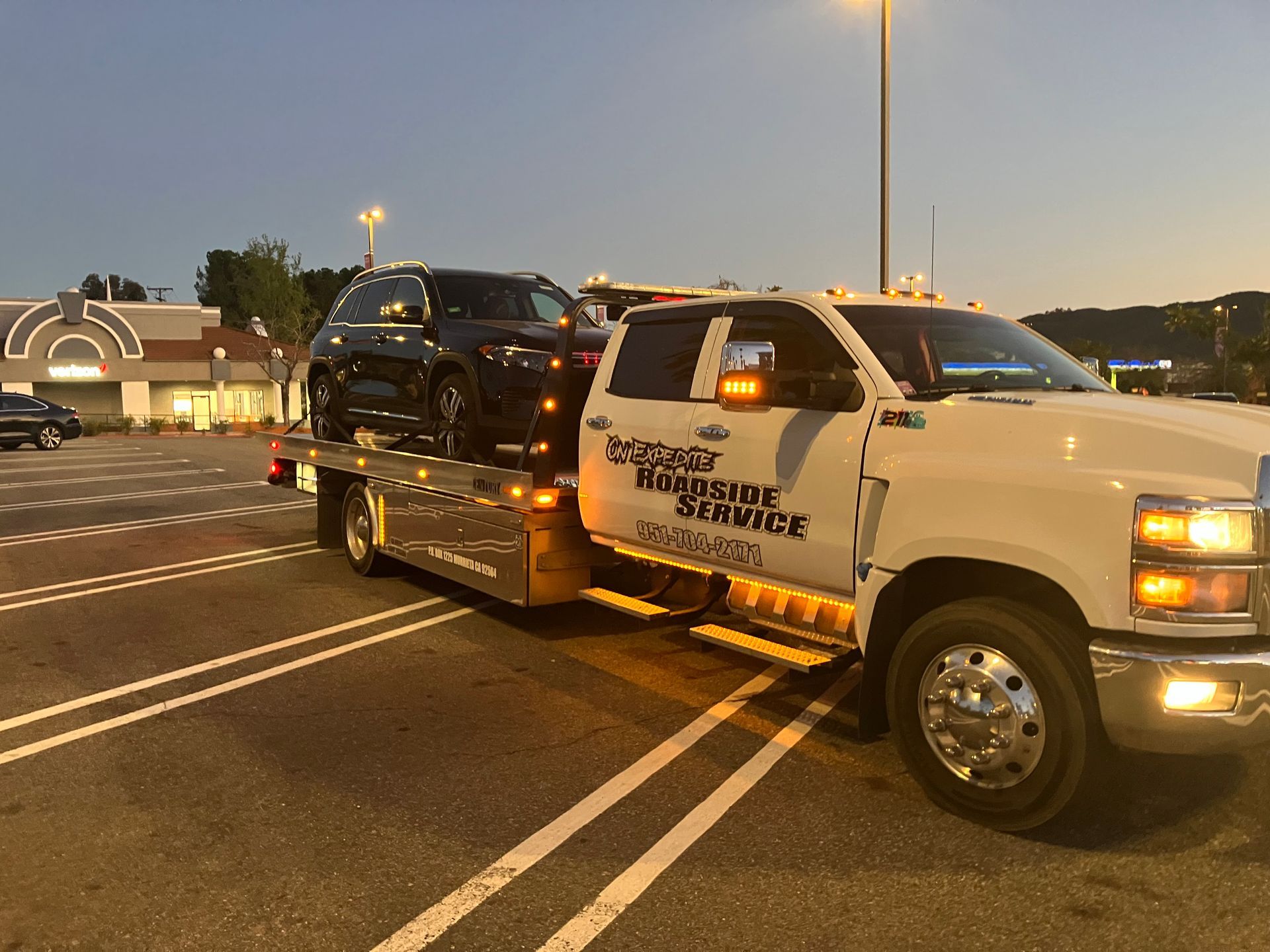 White Smart car being towed on a flatbed tow truck in front of a two-story house.