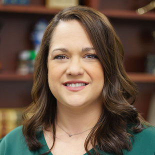 Portrait of a smiling woman with brown hair in a teal top, seated in an office setting