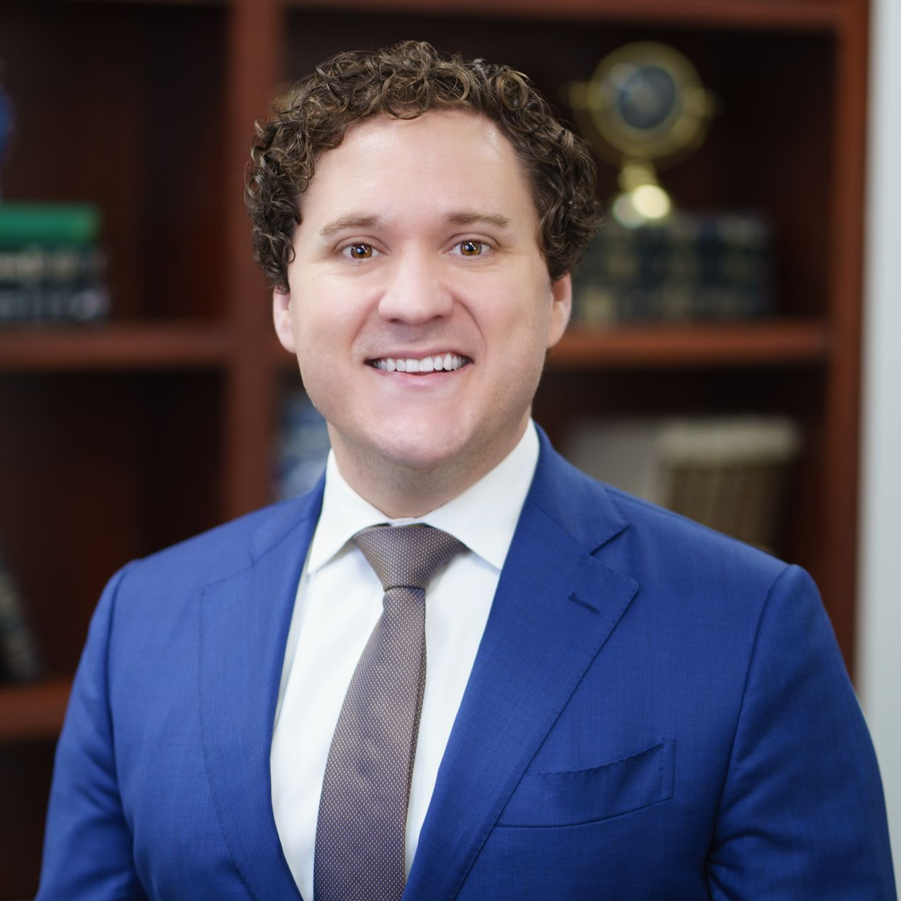Man smiling (Tyler Talbert) l in a blue suit and patterned tie in an office setting