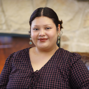 Woman in a dark plaid dress smiling indoors against a blurred background