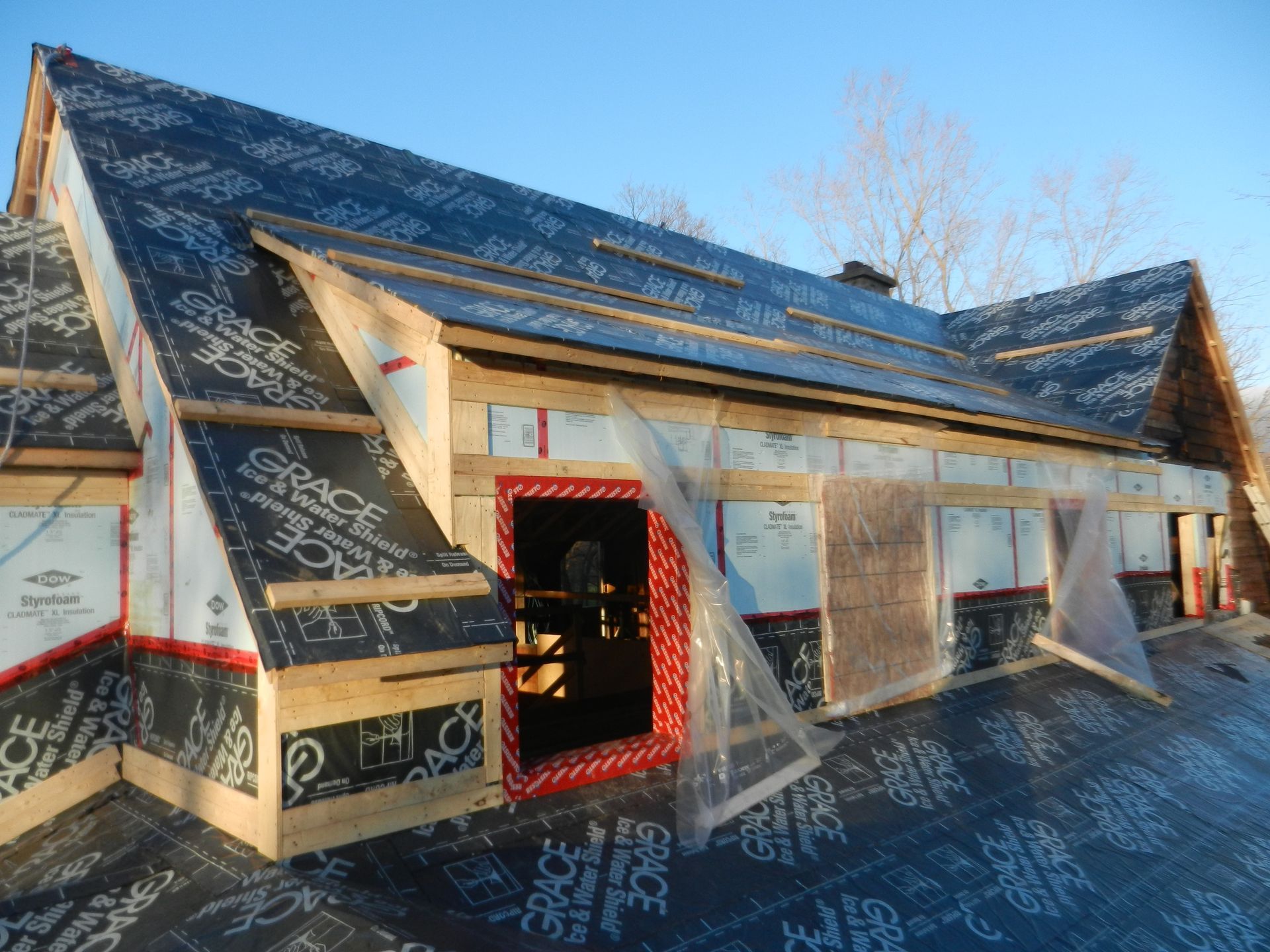 A partially constructed building with a black roof and exposed wooden framing. Plastic sheeting covers some openings.