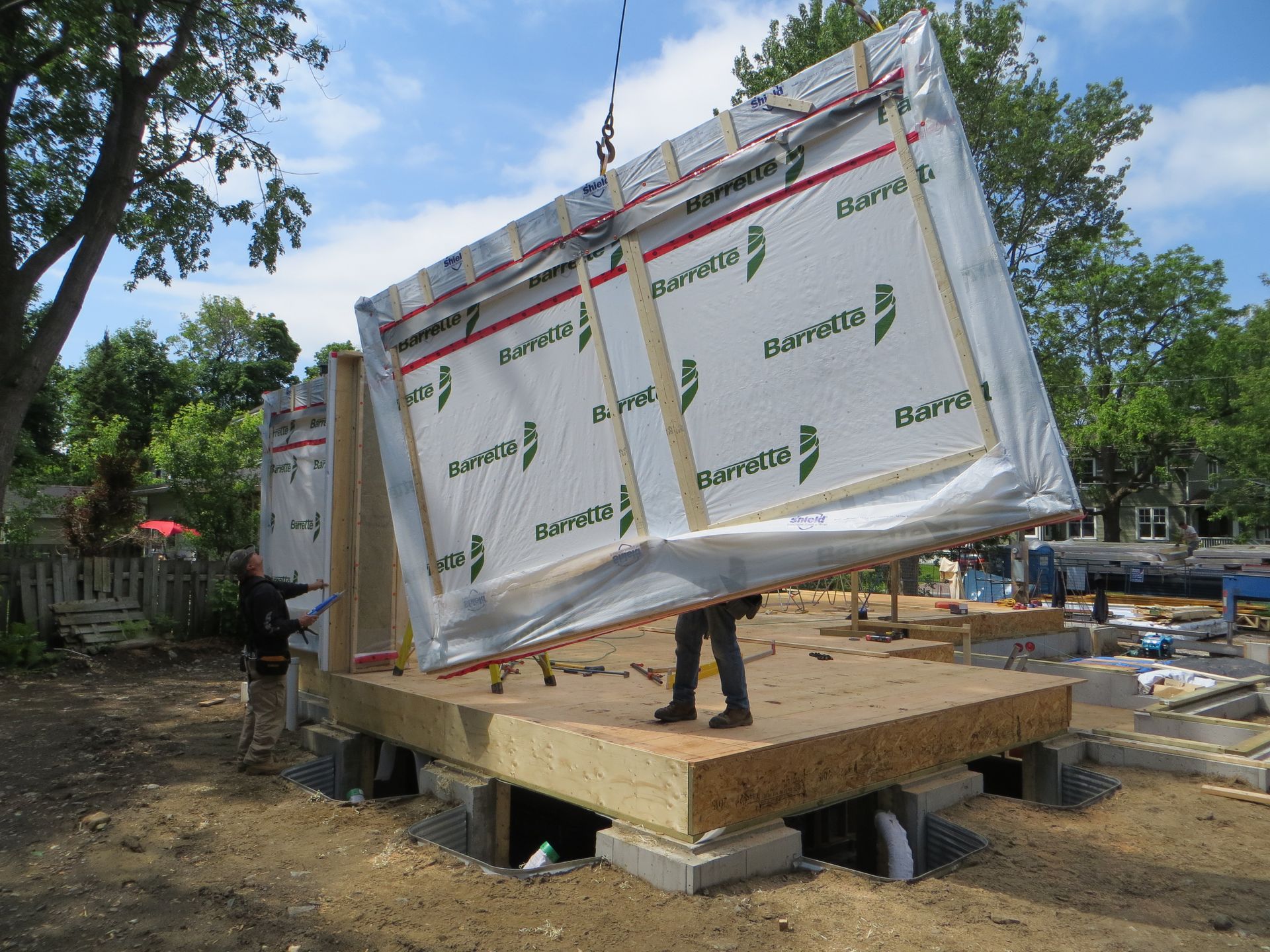 A worker guiding a wall panel being lifted by a crane during modular home construction.