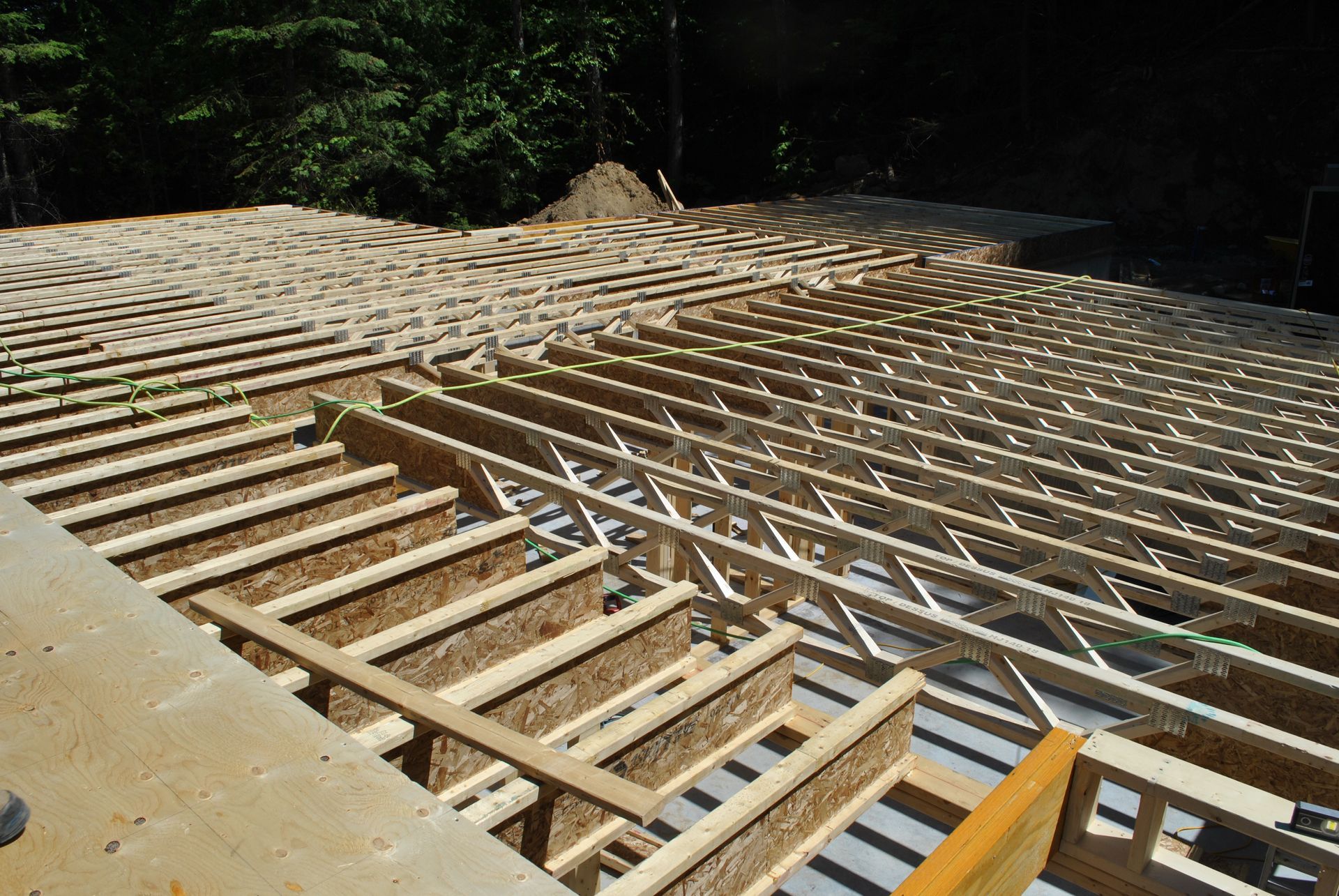 Wooden floor joists being installed on a concrete foundation, outdoors in sunlight.