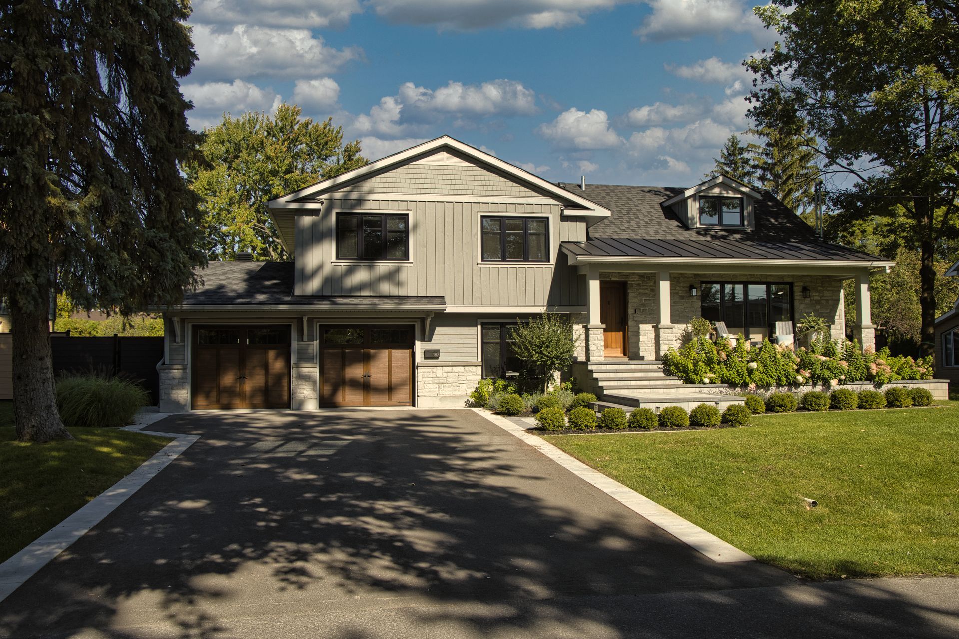 Modern two-story house with gray siding, two-car garage, and a green lawn on a sunny day.