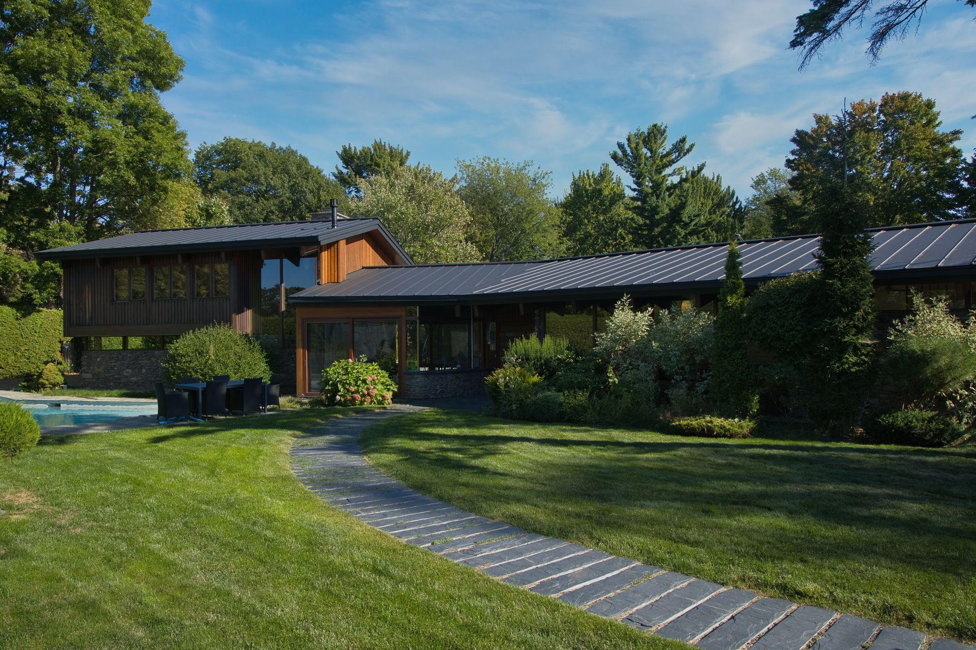 Mid-century modern brown house with dark roof; path through green lawn.