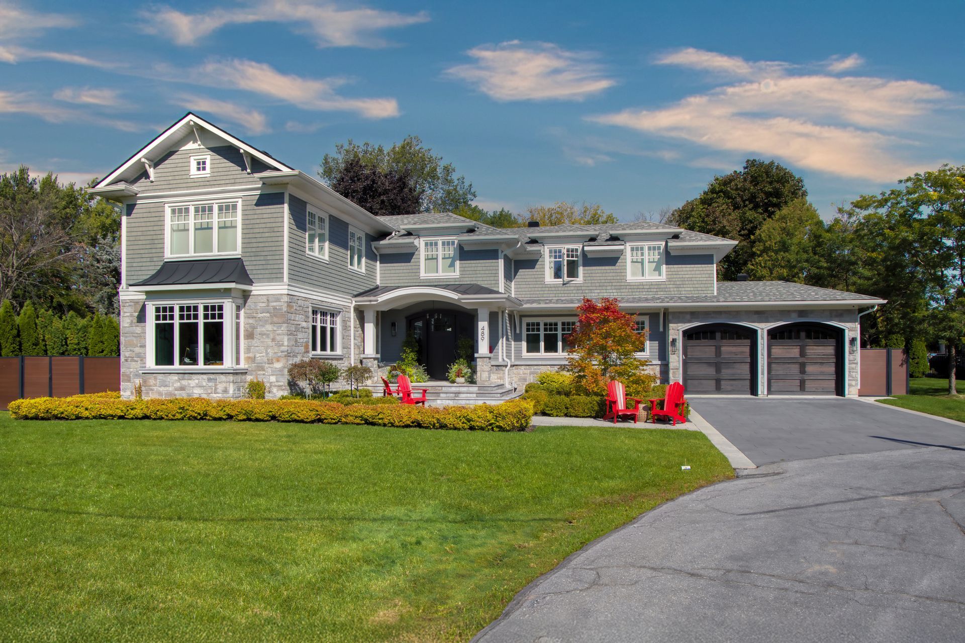 Two-story gray house with stone accents, a lawn, and driveway on a sunny day.