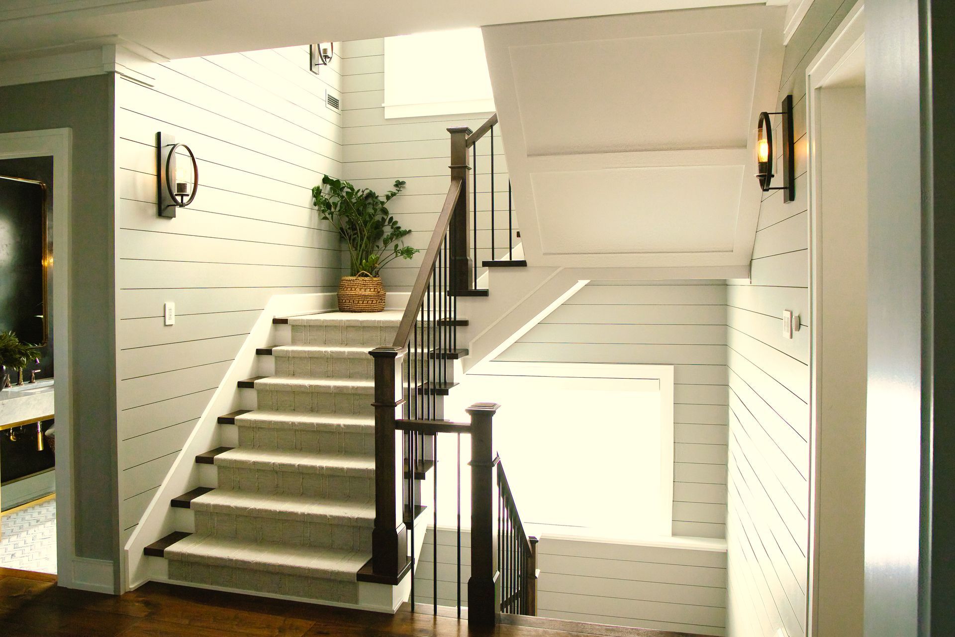 Staircase with light gray walls, dark wood banister, and cream-colored carpet. A potted plant sits on the landing.