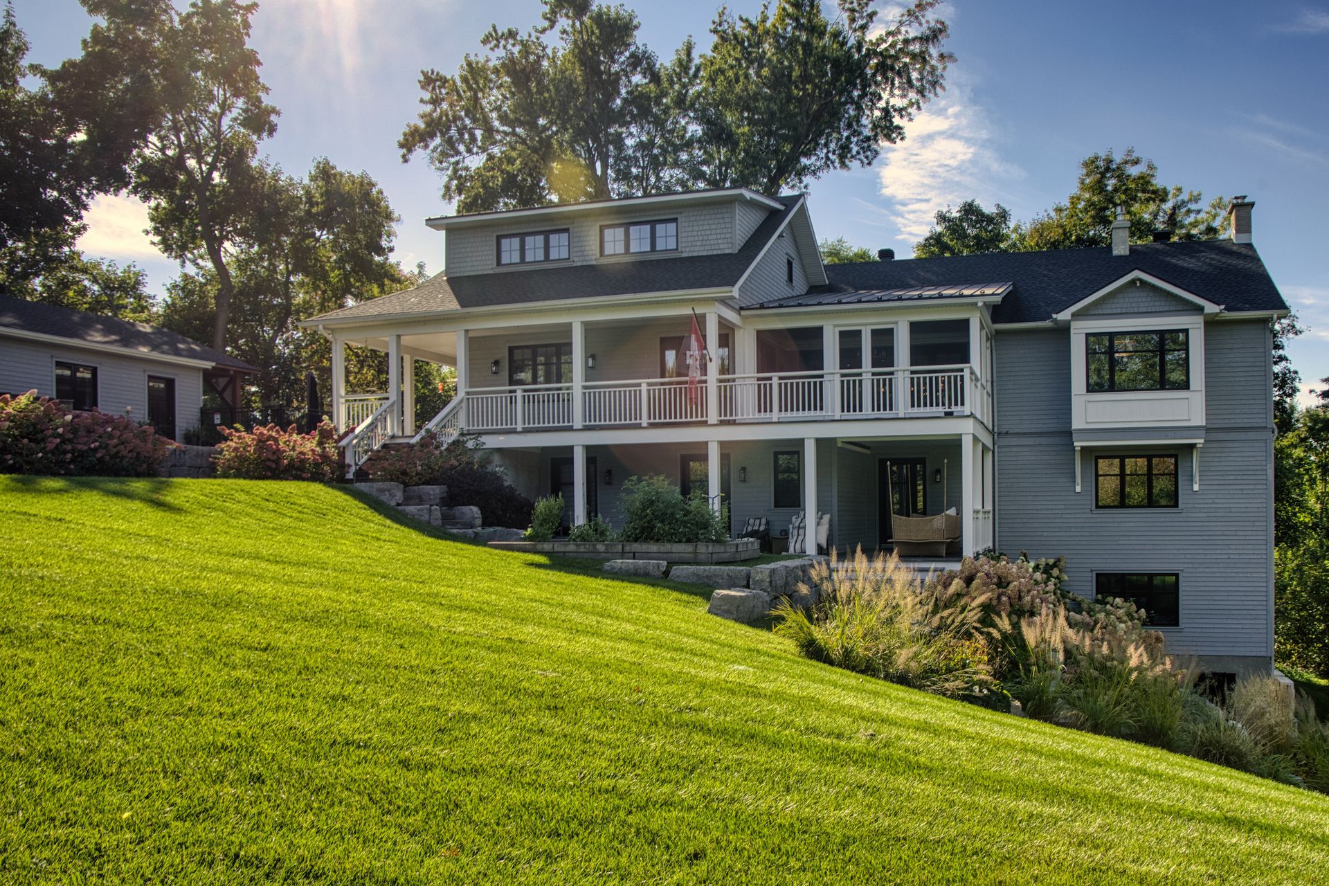 Two-story gray house with porch and lawn on a sunny hillside.