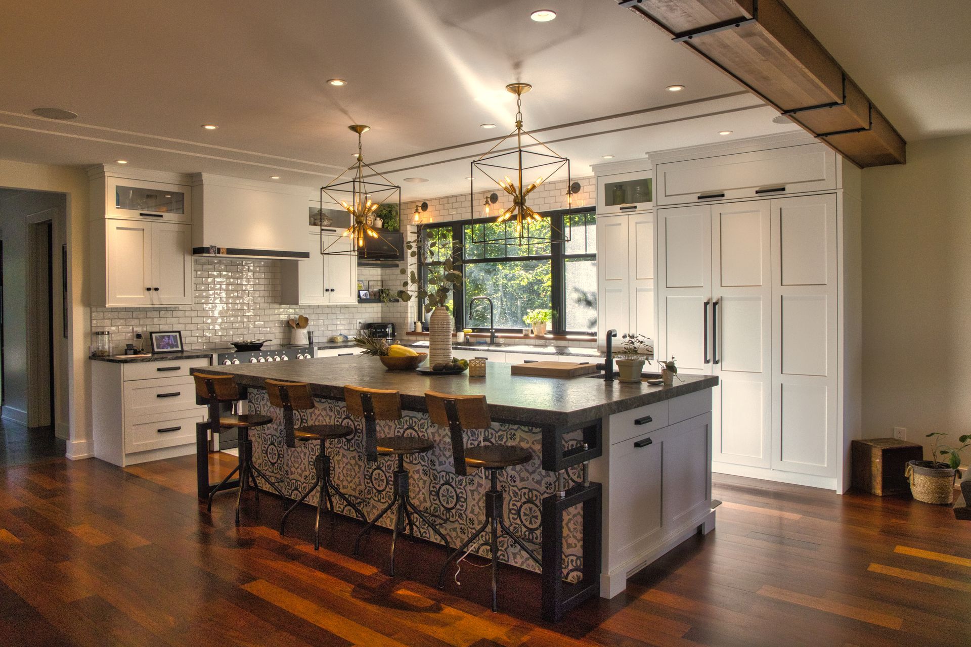 Spacious kitchen with large island, white cabinets, dark wood floors, and two gold pendant lights.