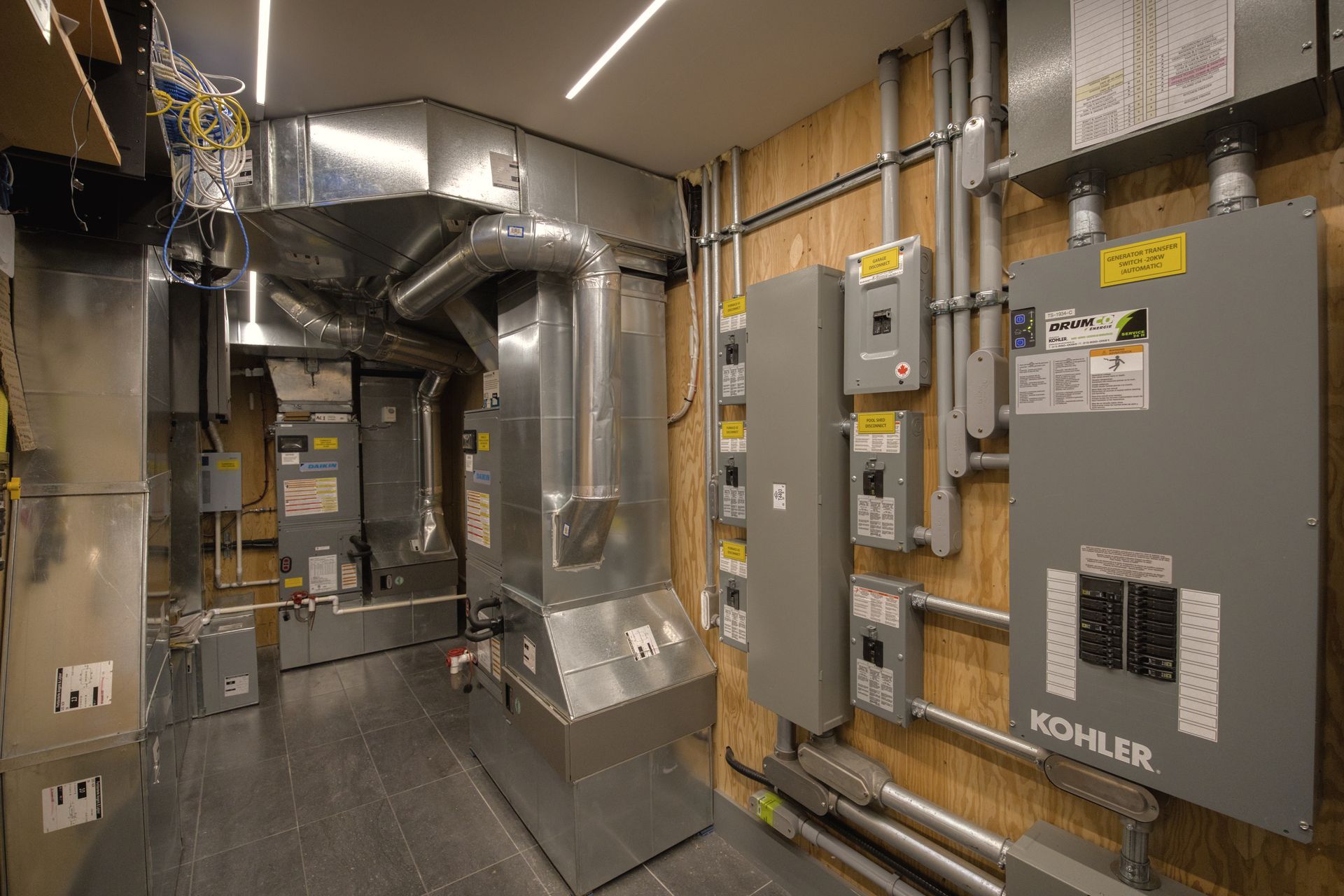 Mechanical room with HVAC ducts, electrical panels, and conduit on wood-paneled walls.