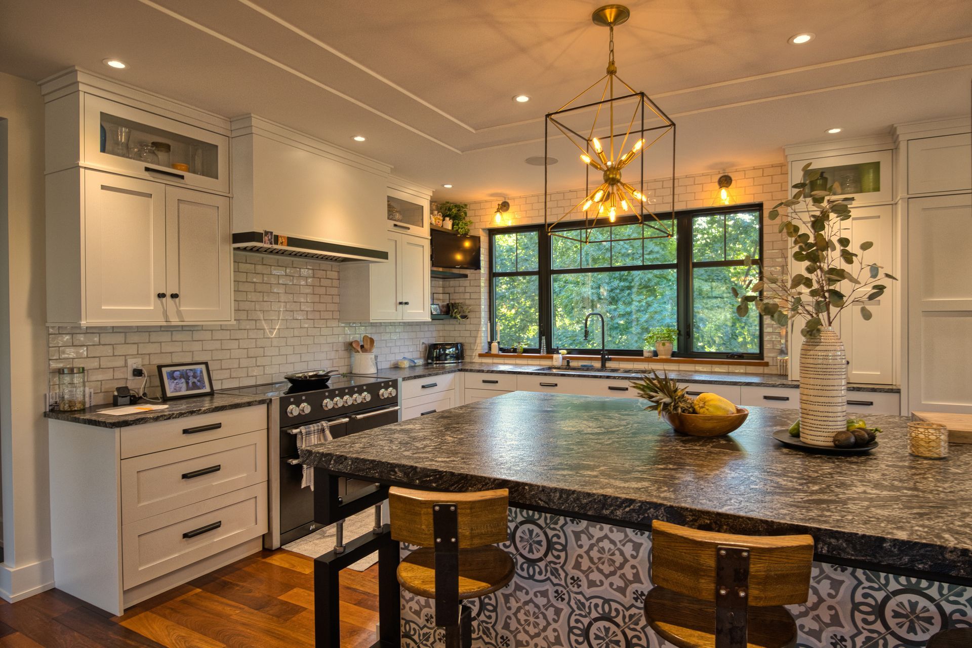 Kitchen with white cabinets, dark countertops, a patterned island, and large window.