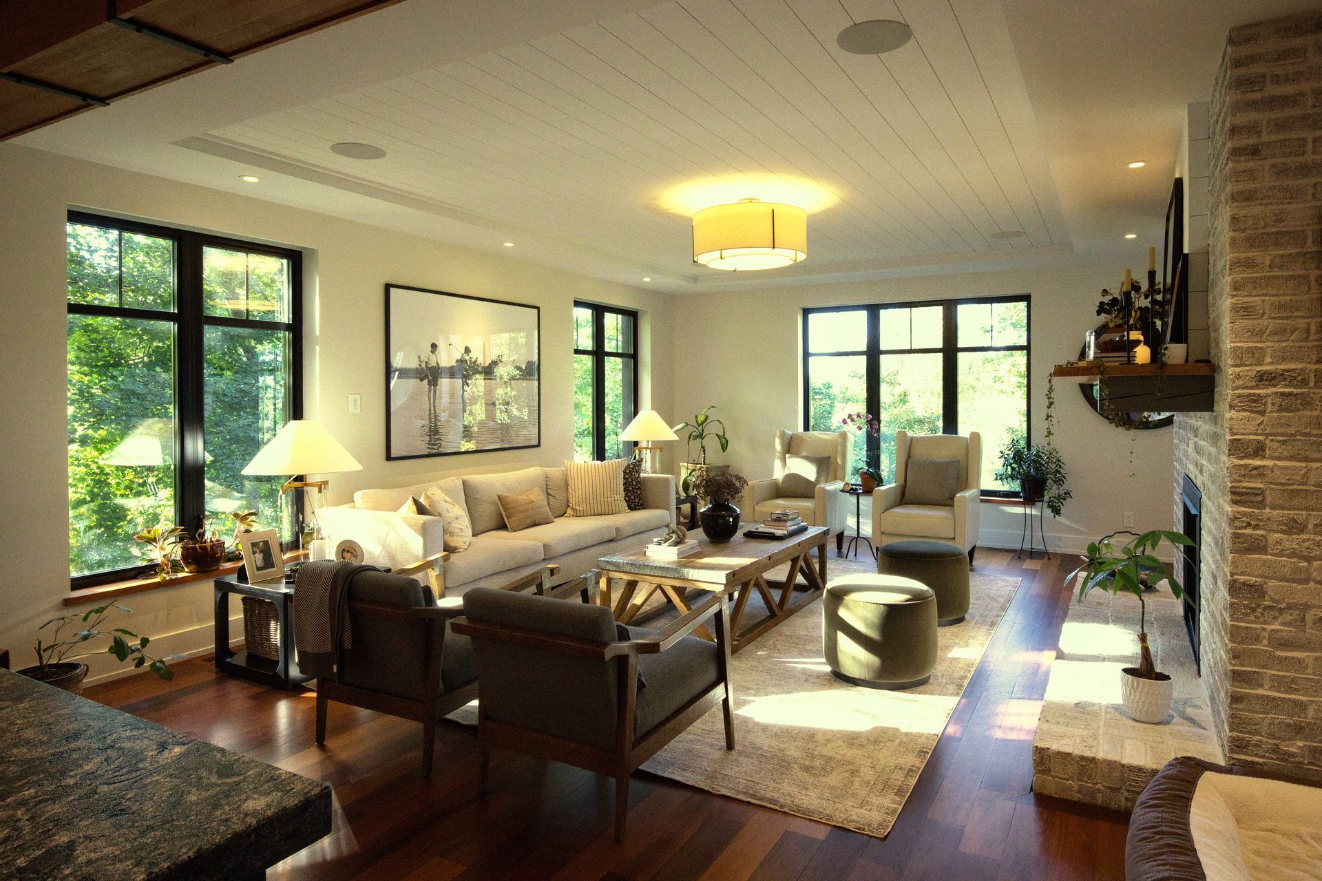 Living room with dark wood floors, large windows, fireplace, and neutral-toned furniture.