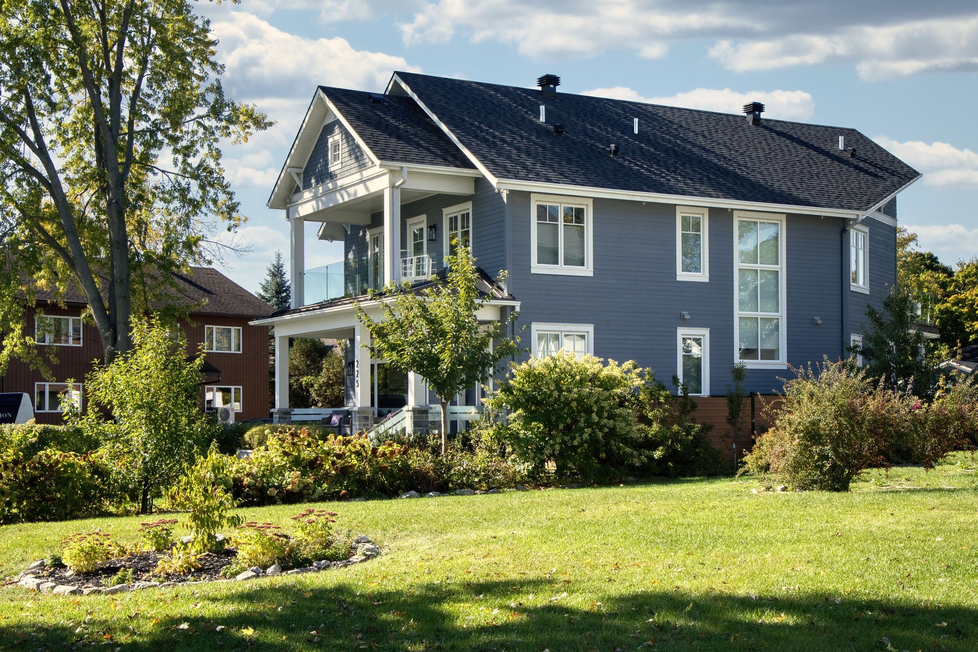 Blue two-story house with a balcony and green lawn under a cloudy sky.