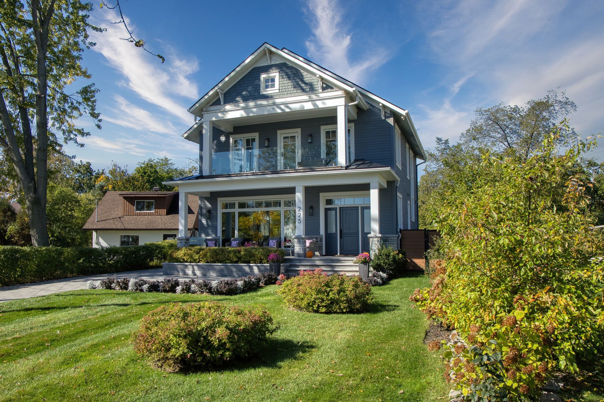 Blue two-story house with white trim, porch, and glass railing, set on a green lawn with a bright blue sky.