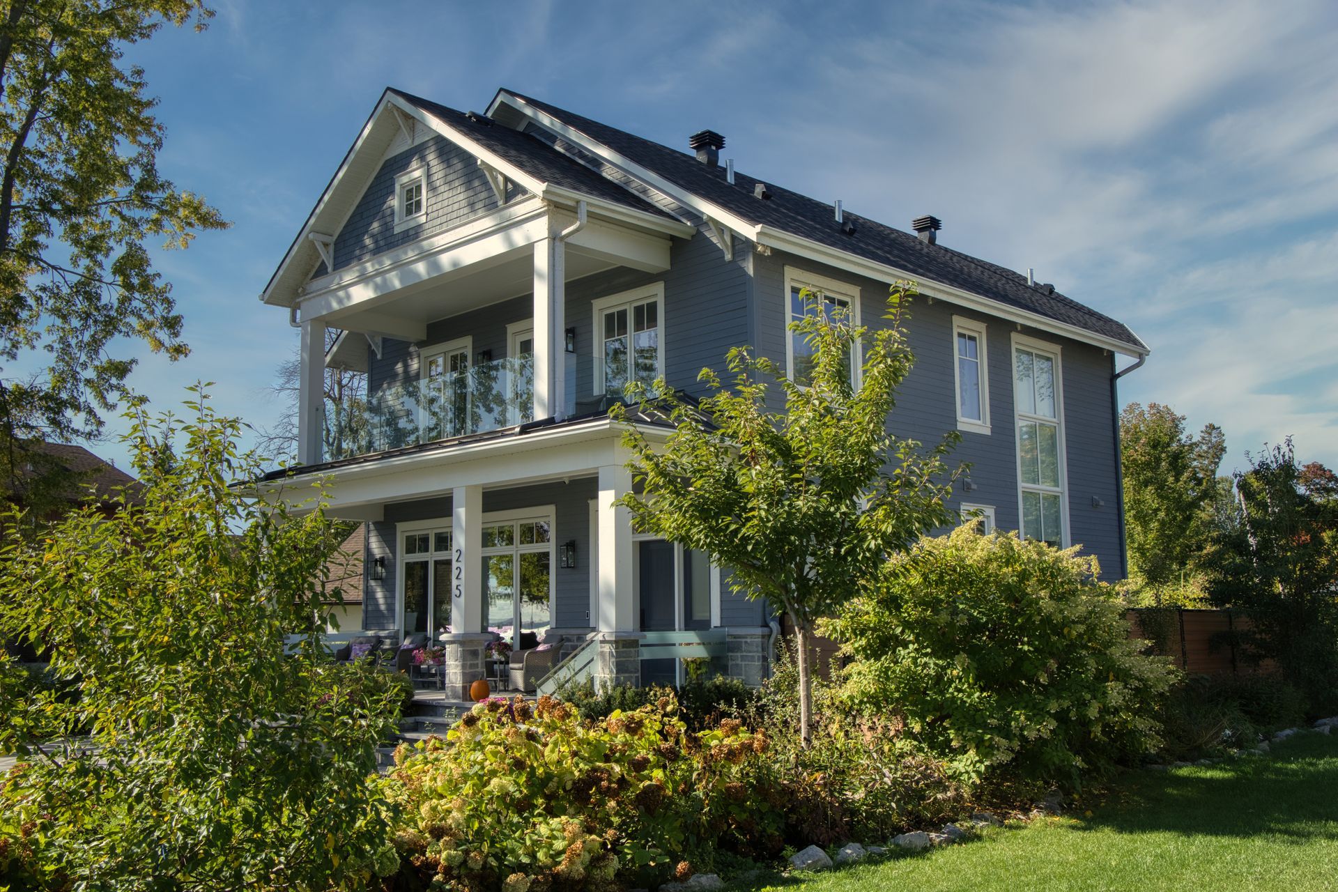 Two-story blue house with white trim, a porch, and glass balcony on a sunny day.
