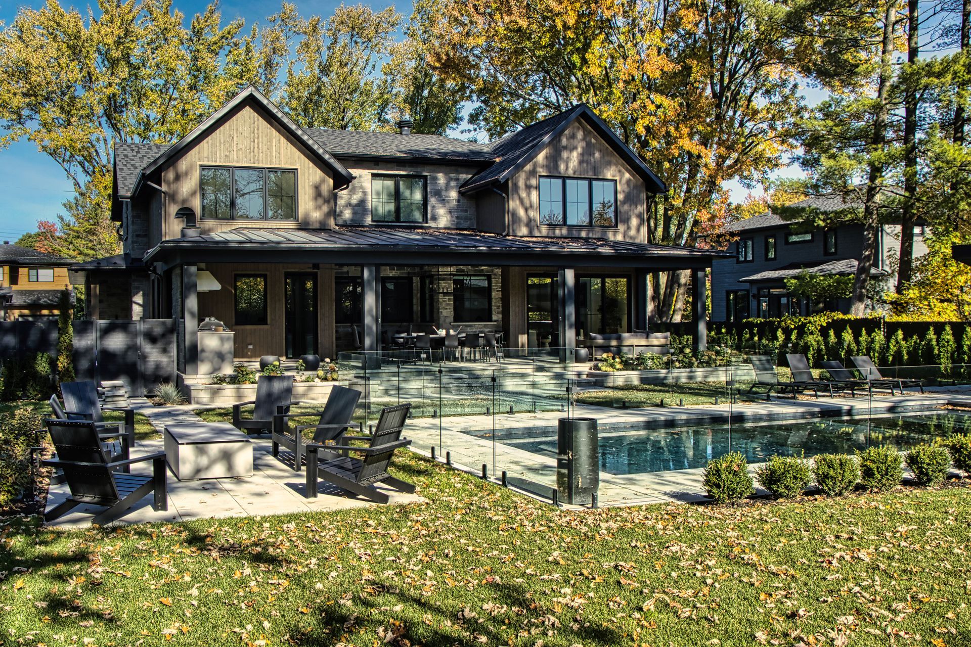 Backyard with a modern house, pool, and seating; autumn foliage.