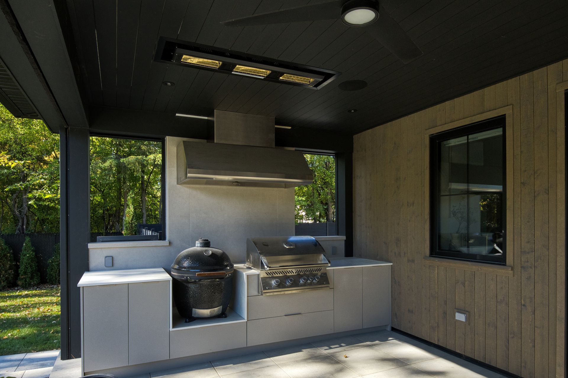 Outdoor kitchen with grill, smoker, and stainless hood under a black ceiling.