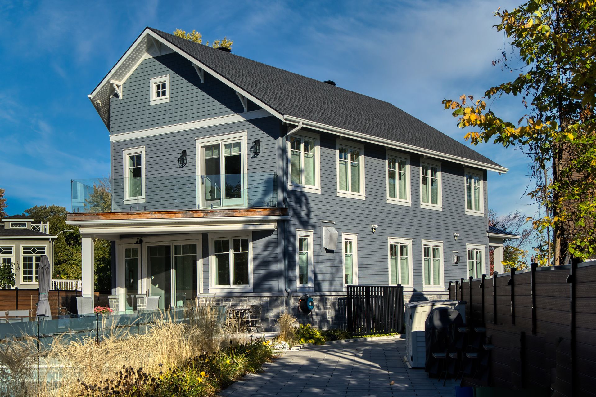 Two-story blue house with white trim, porch, and dark roof. Sunny day with blue sky.
