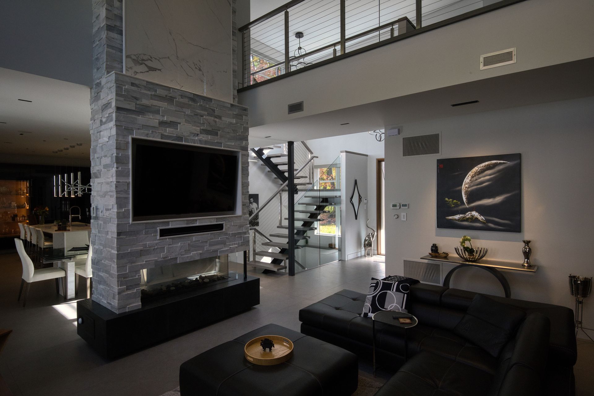 Living room with a large TV, fireplace, and a second-story landing with a staircase visible.