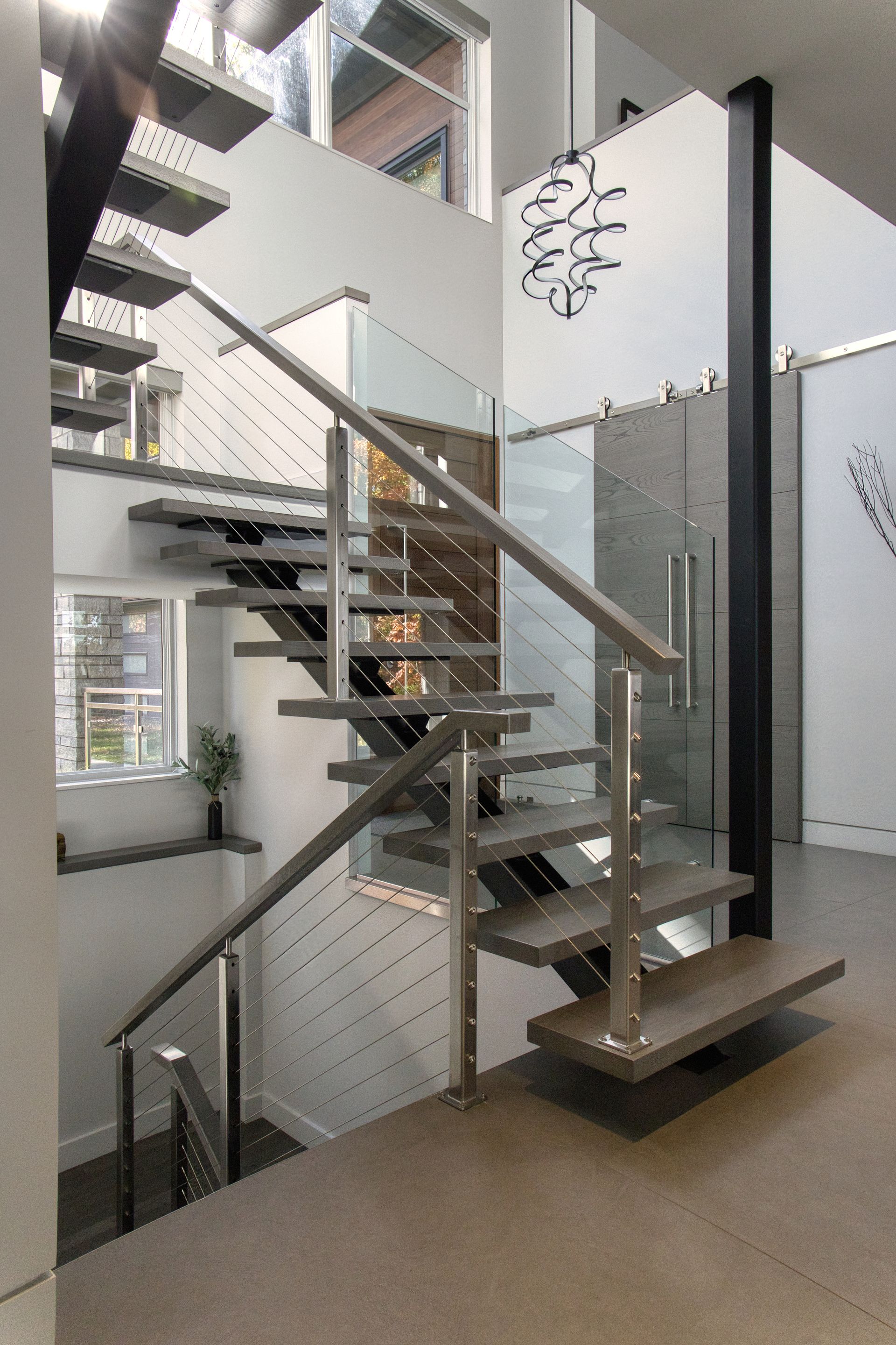 Modern staircase with floating wooden steps, glass and metal railings, and a large black support beam.