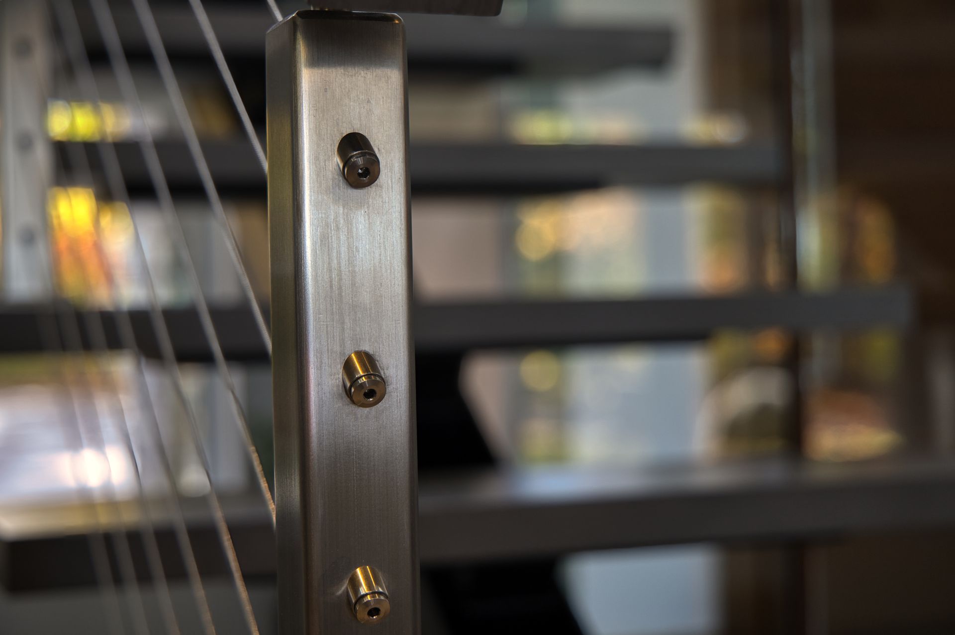 Stainless steel railing post with cable wire. Close-up view with blurred background of shelves.