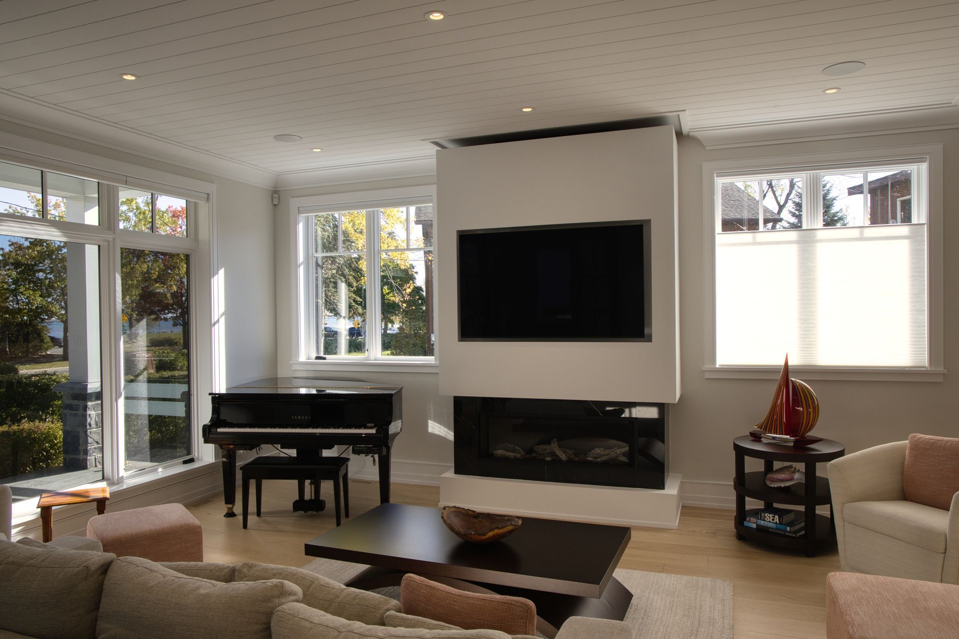Living room with piano, fireplace, TV, and windows; light wood floors, neutral tones.