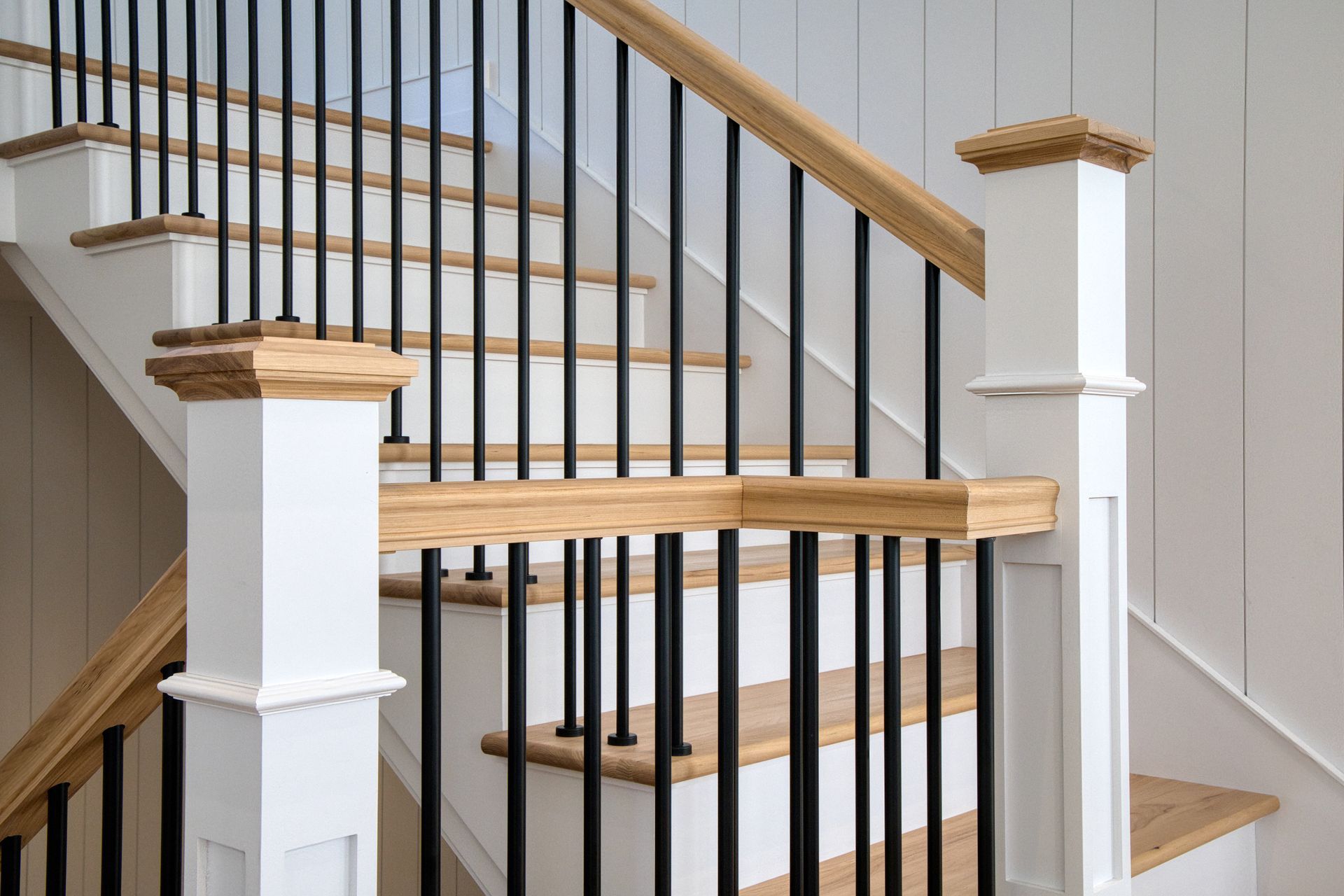 Staircase with wooden steps, white risers, black spindles, and white and wood newel posts.