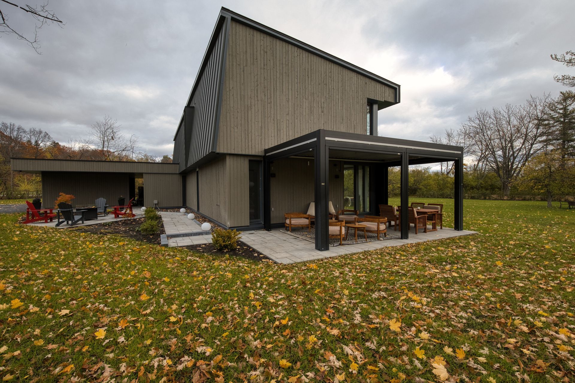 Modern wooden house with angled roof, attached pergola, and autumn lawn.