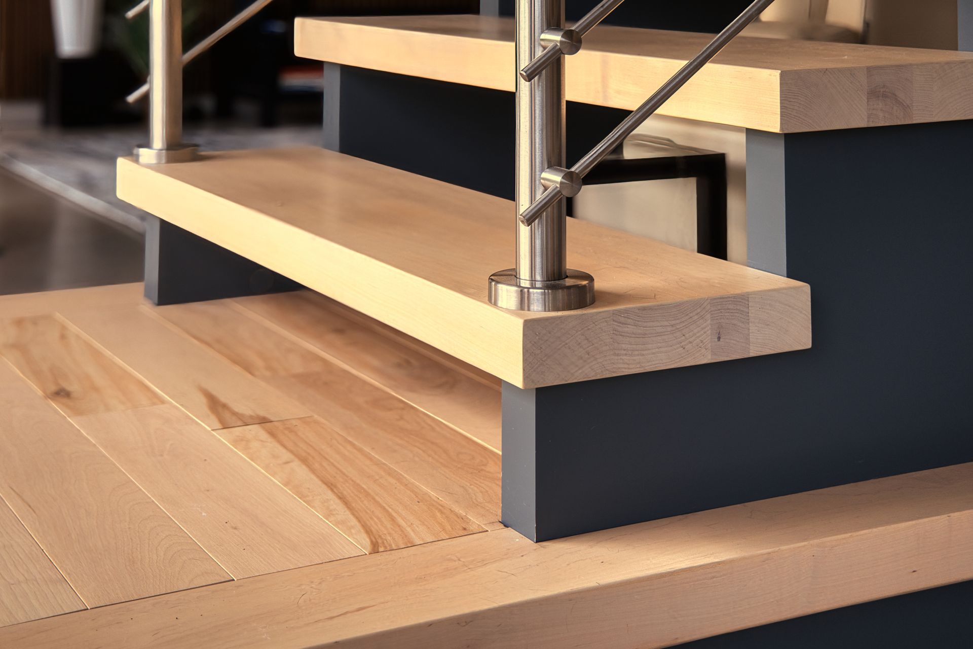 Light wood stairs with metal railing, dark blue risers, and matching hardwood flooring.
