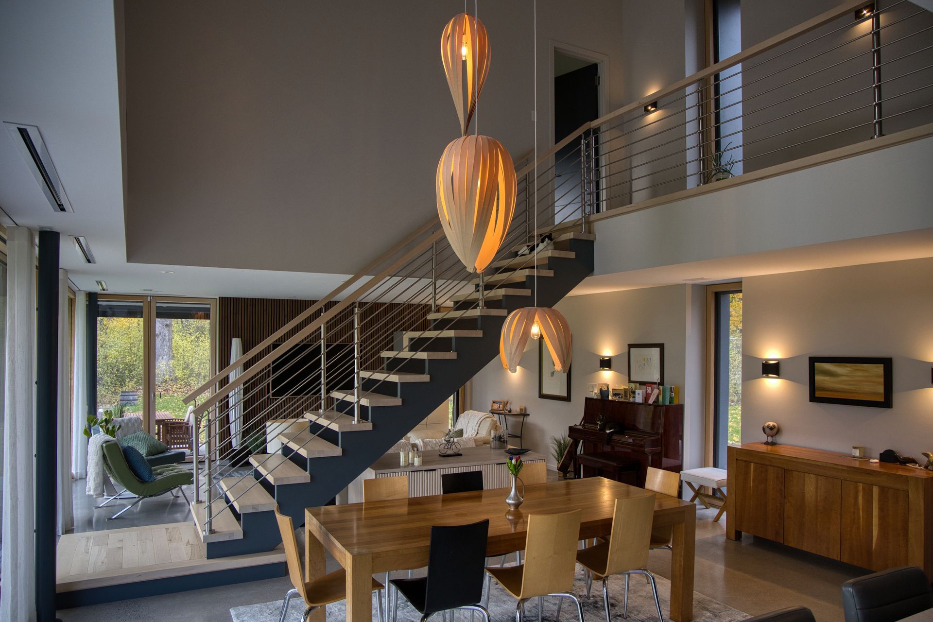 Modern interior with a floating staircase, dining area, and mezzanine, with wood and neutral color tones.