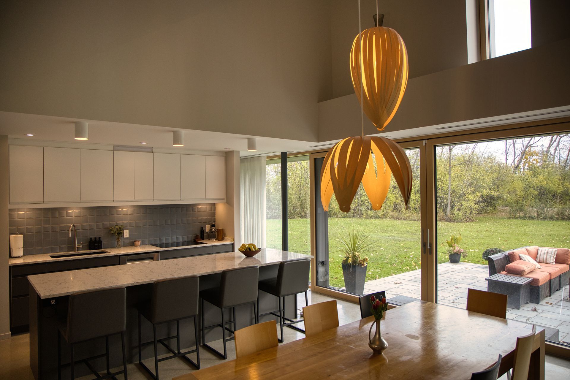 Modern kitchen with island, dining table, and large windows overlooking a patio.