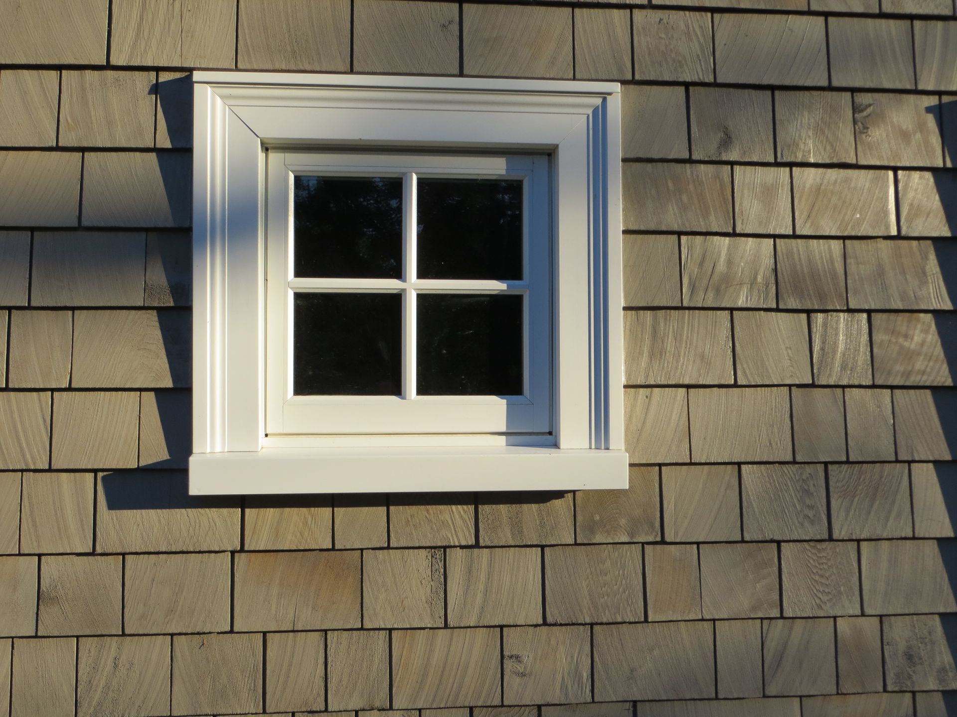 White framed window on a cedar shingled wall.