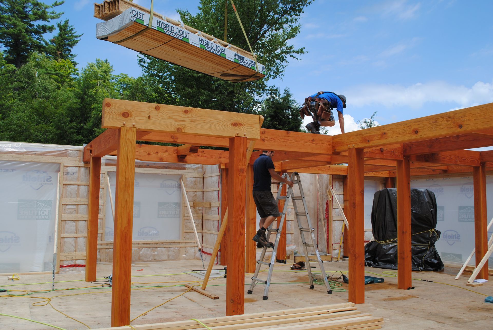 Construction workers lift a wooden beam into place on a partially built building frame.
