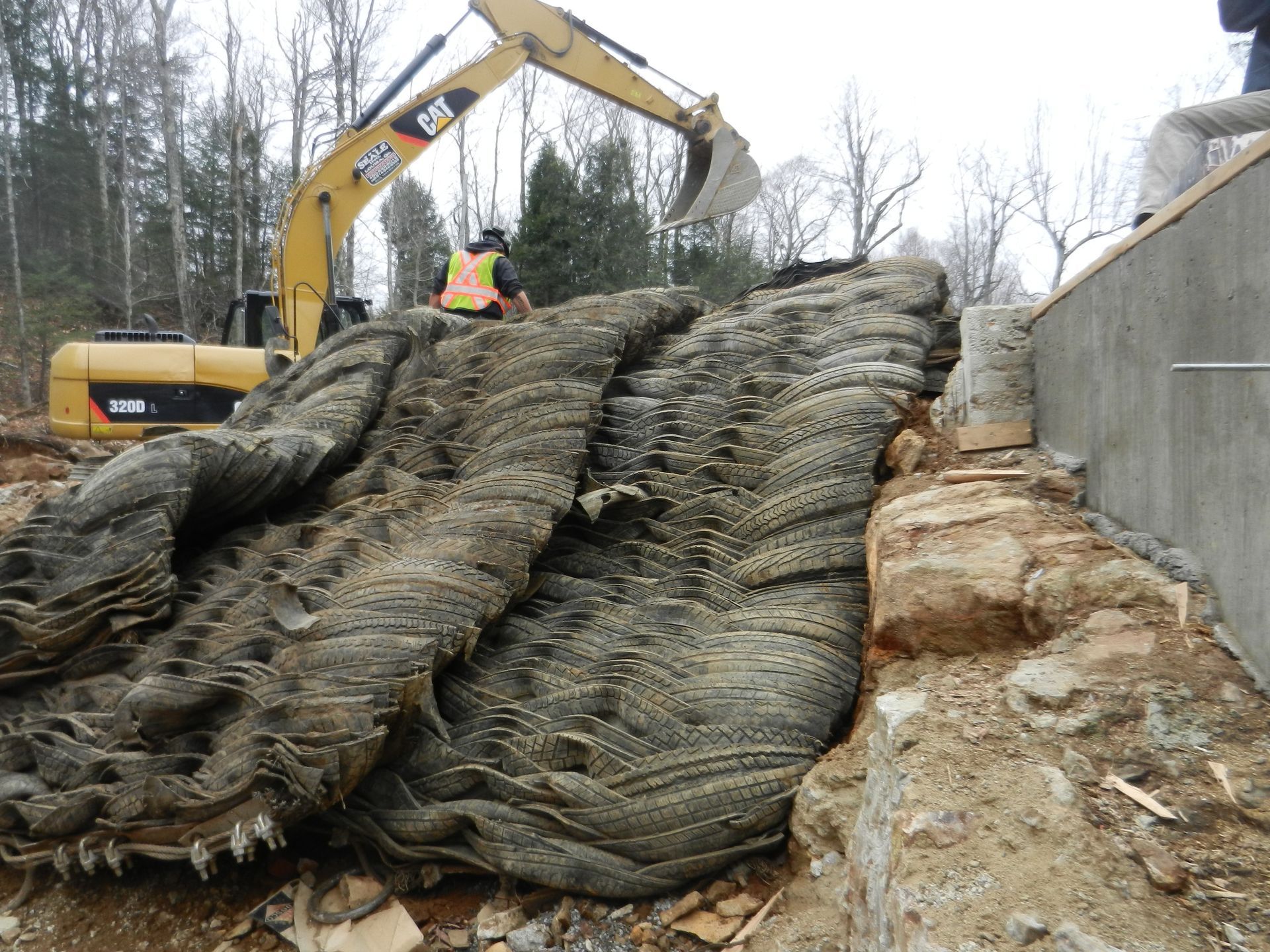 Yellow excavator removing erosion control blanket at construction site.
