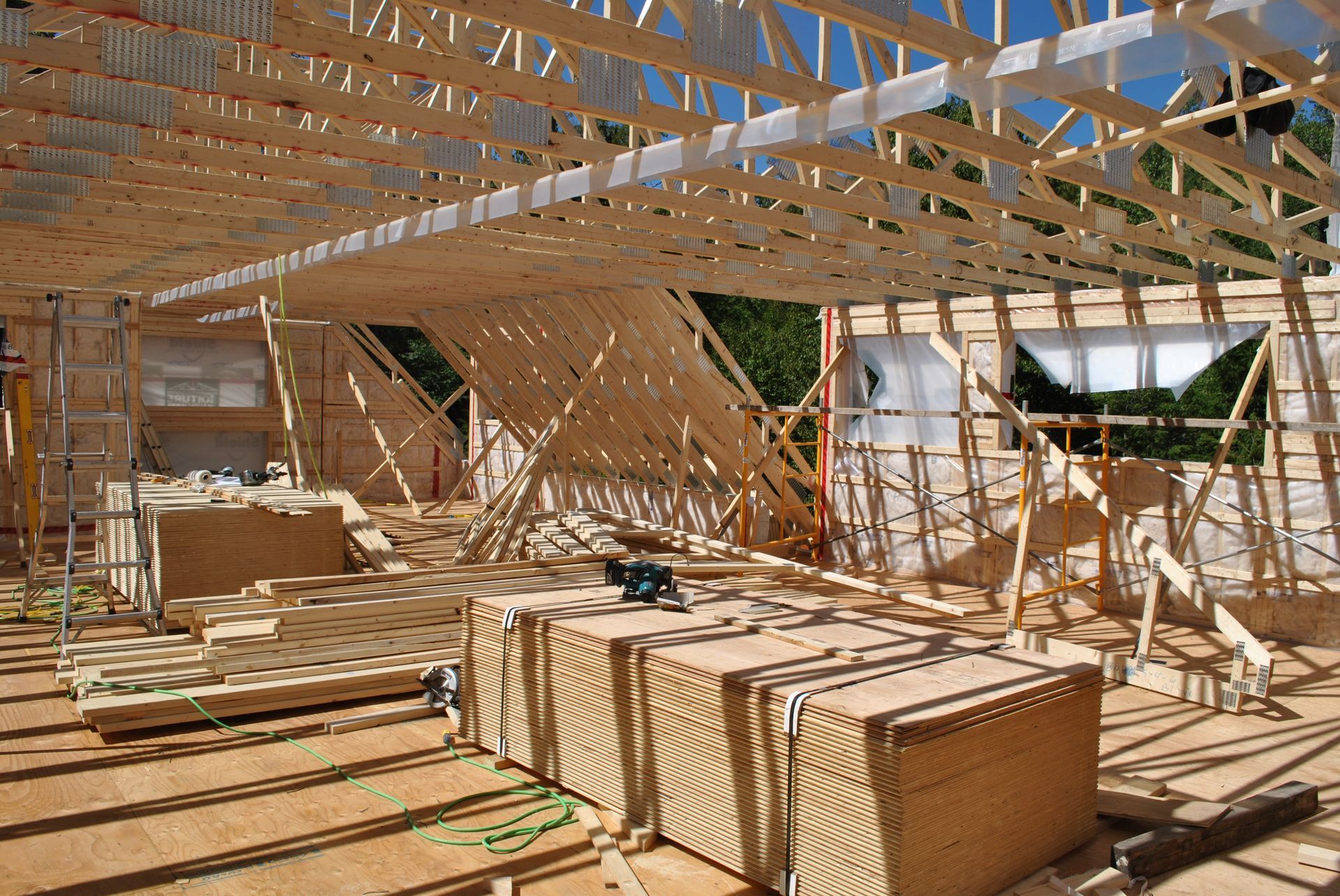 Interior view of a building under construction, wooden framework, stacks of building materials, bright sunlight.
