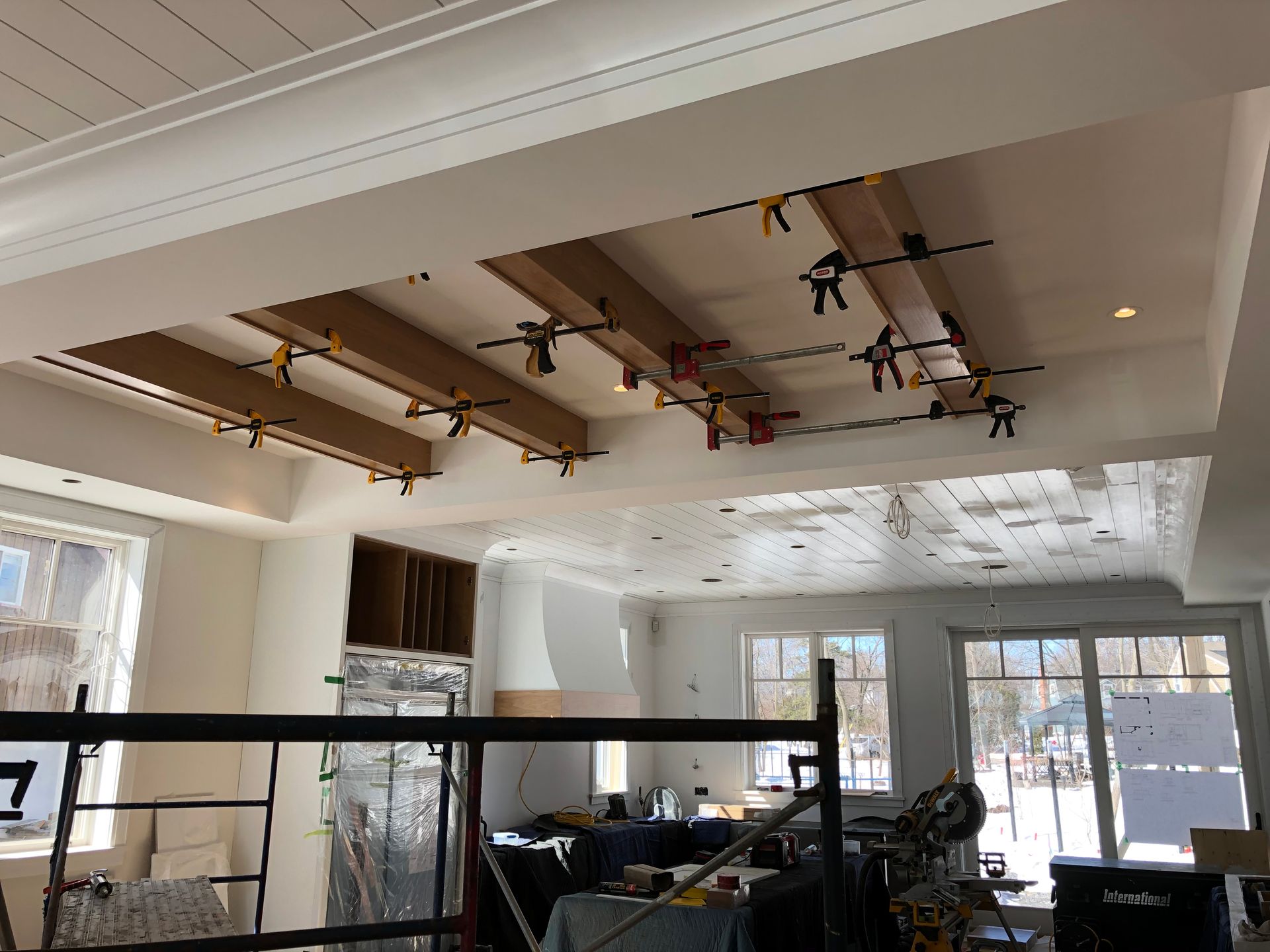 Construction site with wood beams clamped to a white ceiling. Scaffolding and windows are visible.