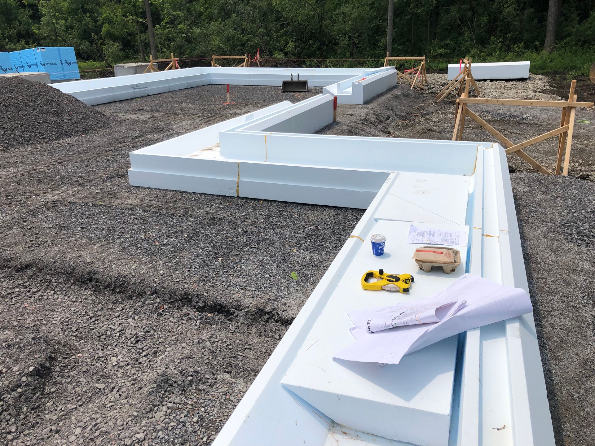 Foundation construction site with white foam blocks, tools, and blueprints on gravel.