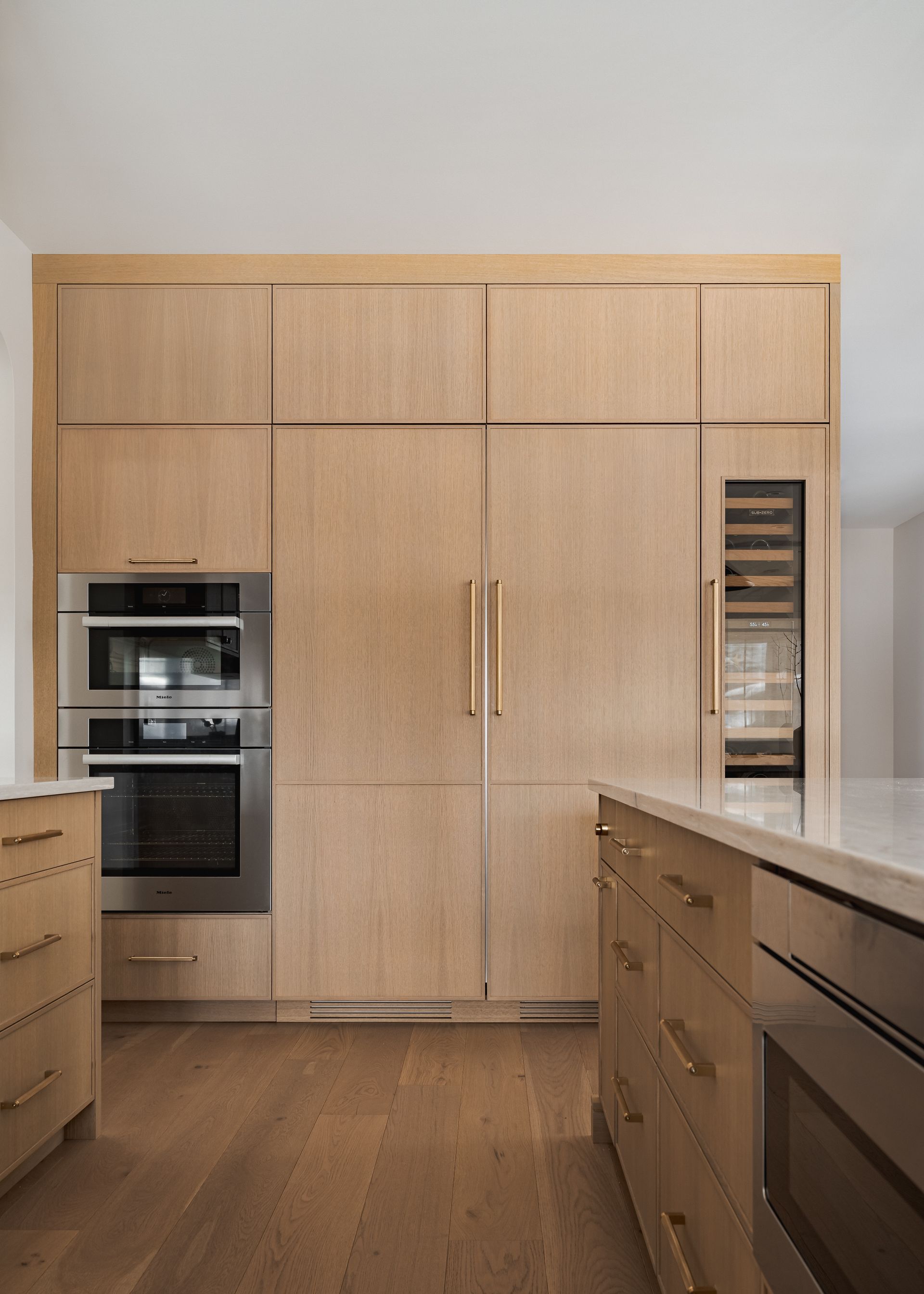 Modern kitchen with light wood cabinetry, built-in ovens, and a wine cooler.