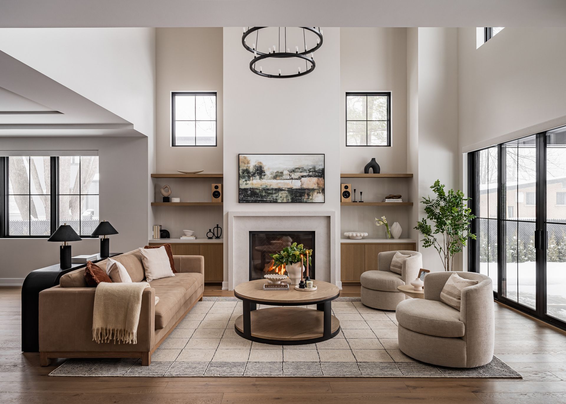Spacious, neutral-toned living room with fireplace, built-in shelving, two armchairs, sofa, and a large rug.
