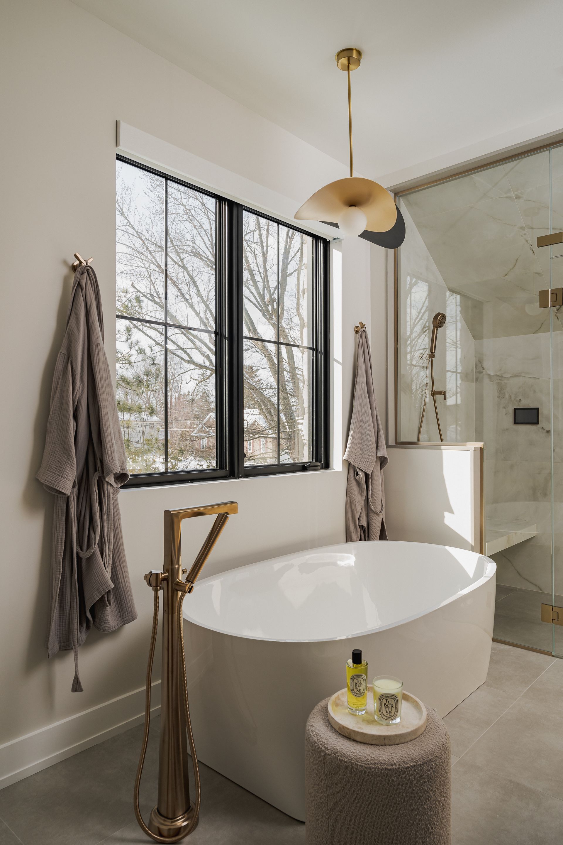 Bathroom with a freestanding tub, gold fixtures, and a window. Two bathrobes hang nearby.