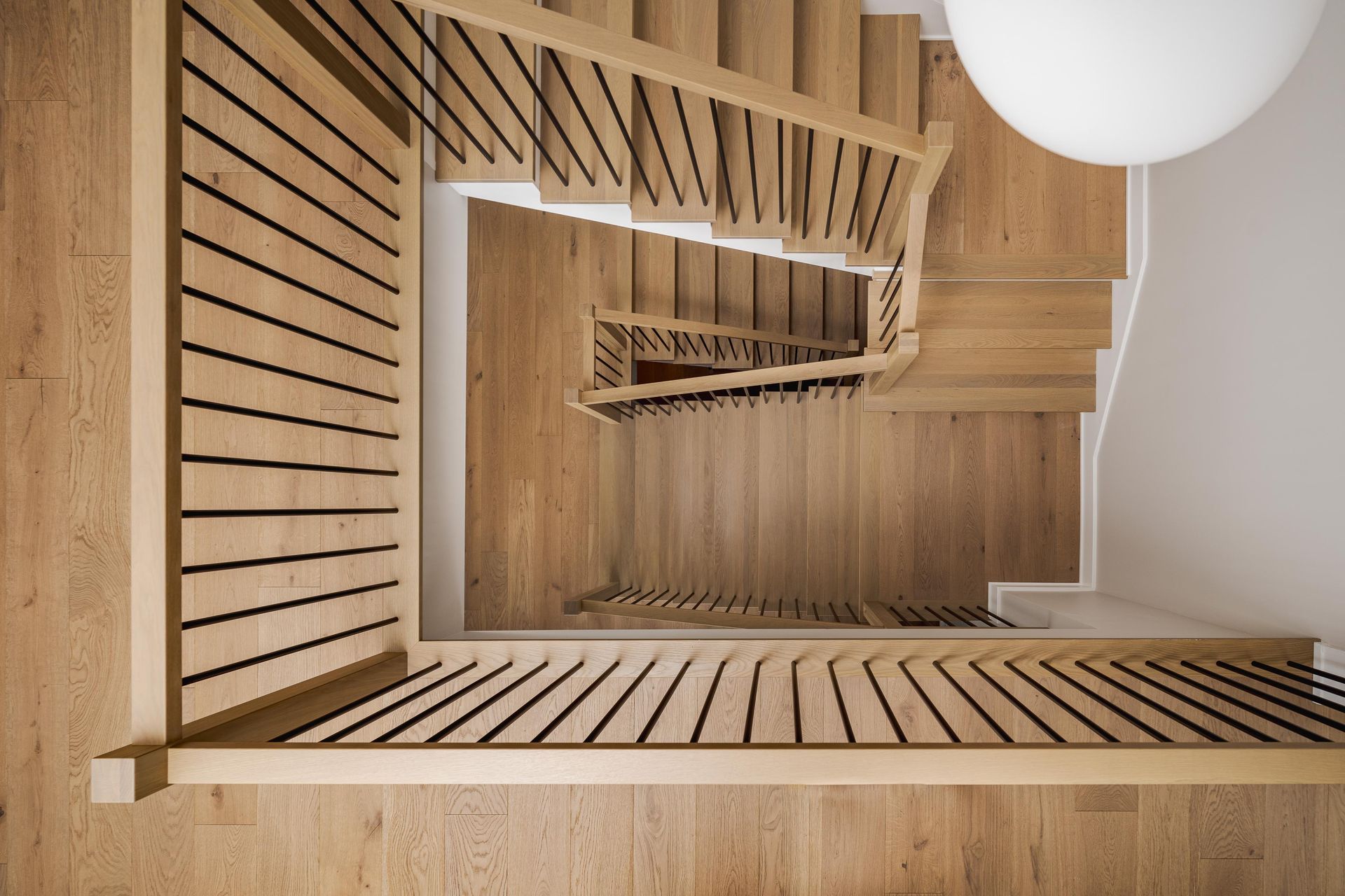 Overhead view of a wooden staircase with black horizontal railings. A white light fixture is in the upper right.