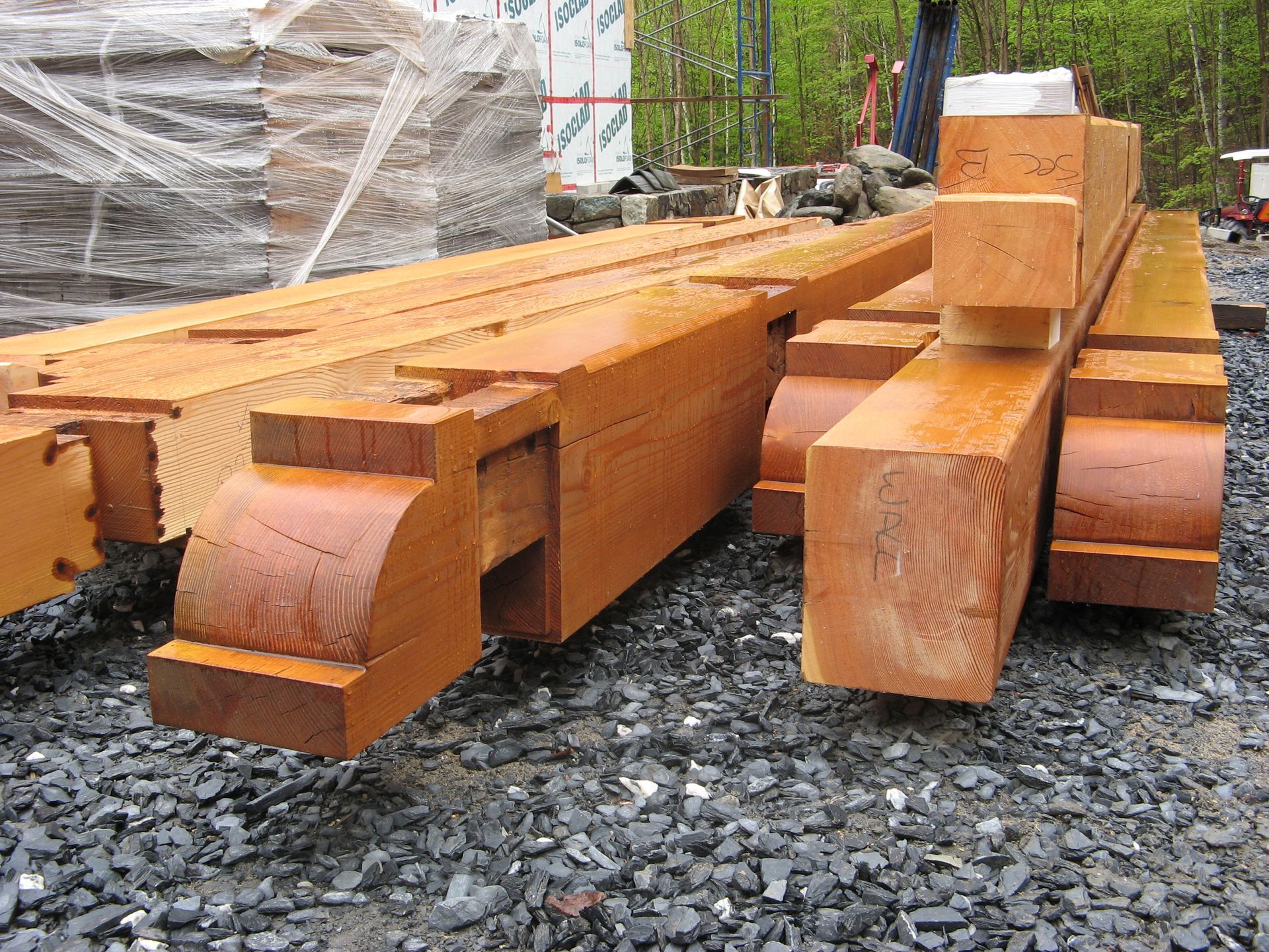 Wooden beams, cut with decorative ends, lie on gravel outdoors.